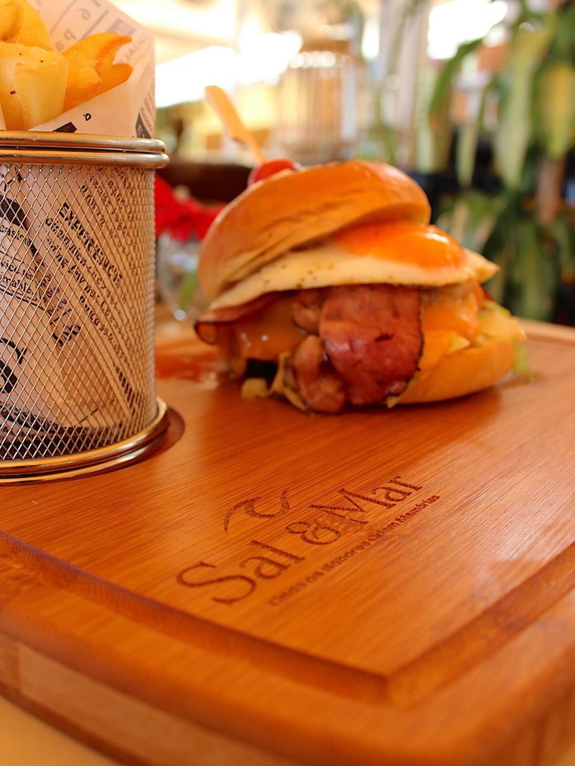 Burger e batatas fritas servidos em tábua com a marca da casa