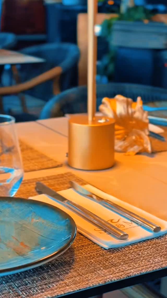 Mesa posta no interior do Sal & Mar, com prato azul, candeeiro dourado e guardanapo da casa